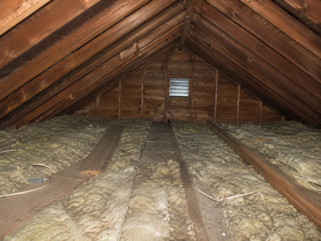 An attic with thin, dark, settled batt insulation between exposed joists in an older home