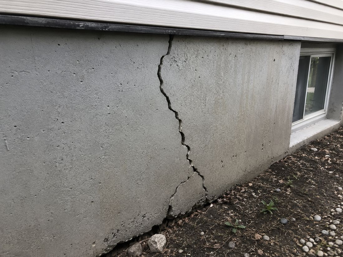 A stepped vertical crack running the full height of a poured concrete foundation wall, photographed before repair